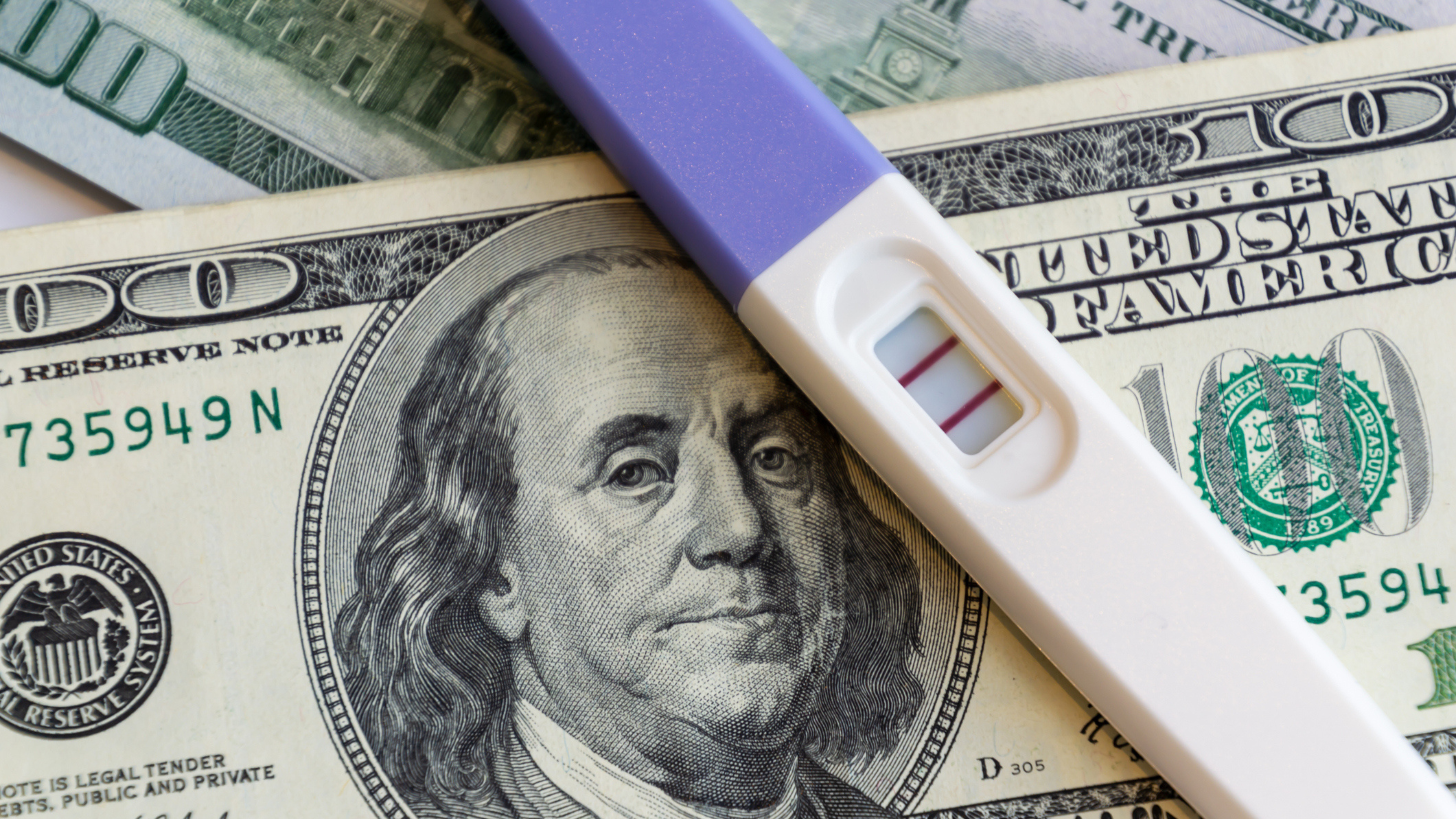 Pregnancy test on cash illustrating the financial burden and uncovered costs of IVF treatment.